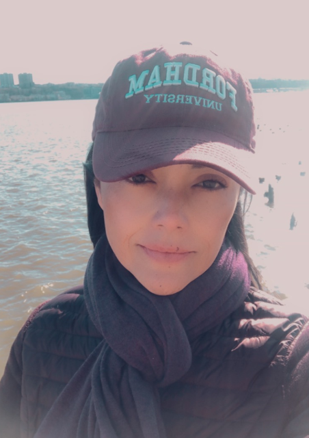 Shenae, wearing a baseball cap from her alma mater Fordham University, standing in front of a body of water